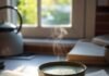 The Best Books About Tea Culture Around the World A flat lay of the book next to a steaming matcha bowl on a messy kitchen counter — natural light streaming in